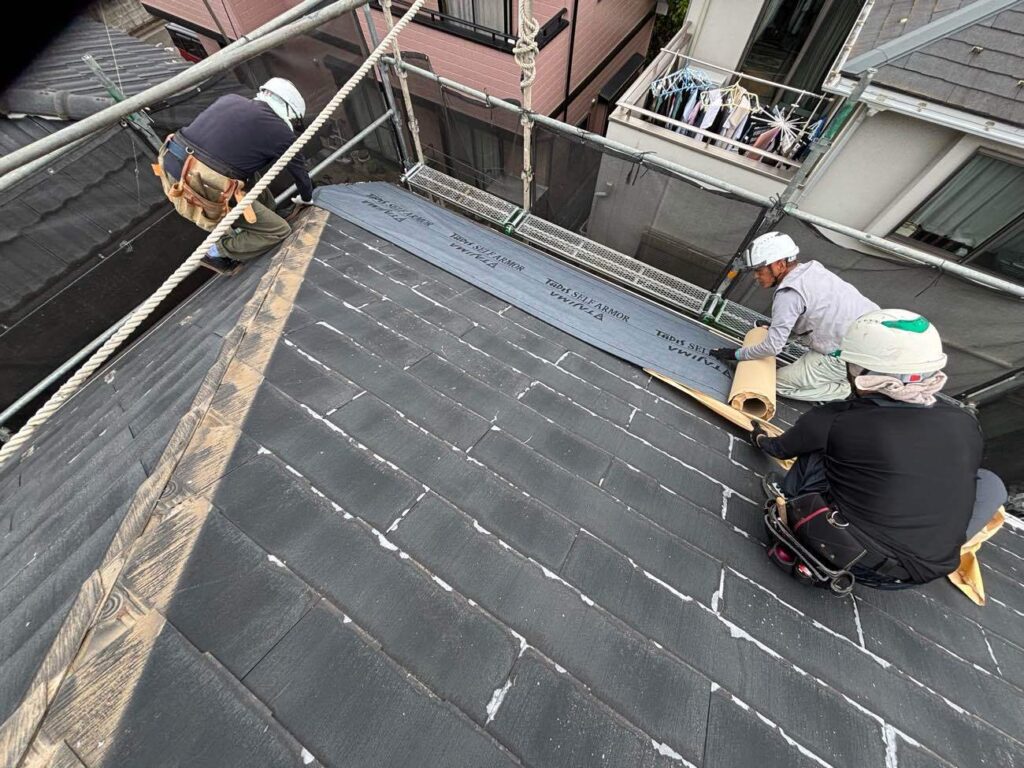 既存屋根の棟板金撤去後、防水紙を設置している様子です。ユウマペイントが使用する防水紙は自着式の「タディスセルフアーマー」です。「アスファルトフェルト」や「アスファルトルーフィング」等の防水紙は施工方法が防水紙をタッカー（大型のホッチキスに似たもの）を使いステーブル（コの字型の針）で固定する「タッピング工法」です。この工法は経年劣化によりシートが縮むため、固定しているところから裂け、そこから雨水が浸入する恐れがあります。ユウマペイントでは、数ある防水紙・工法の中から「どの防水紙をどのような工法で設置していくことがお客様の建物を守ることにつながるのか」という視点でご提案をしております。
