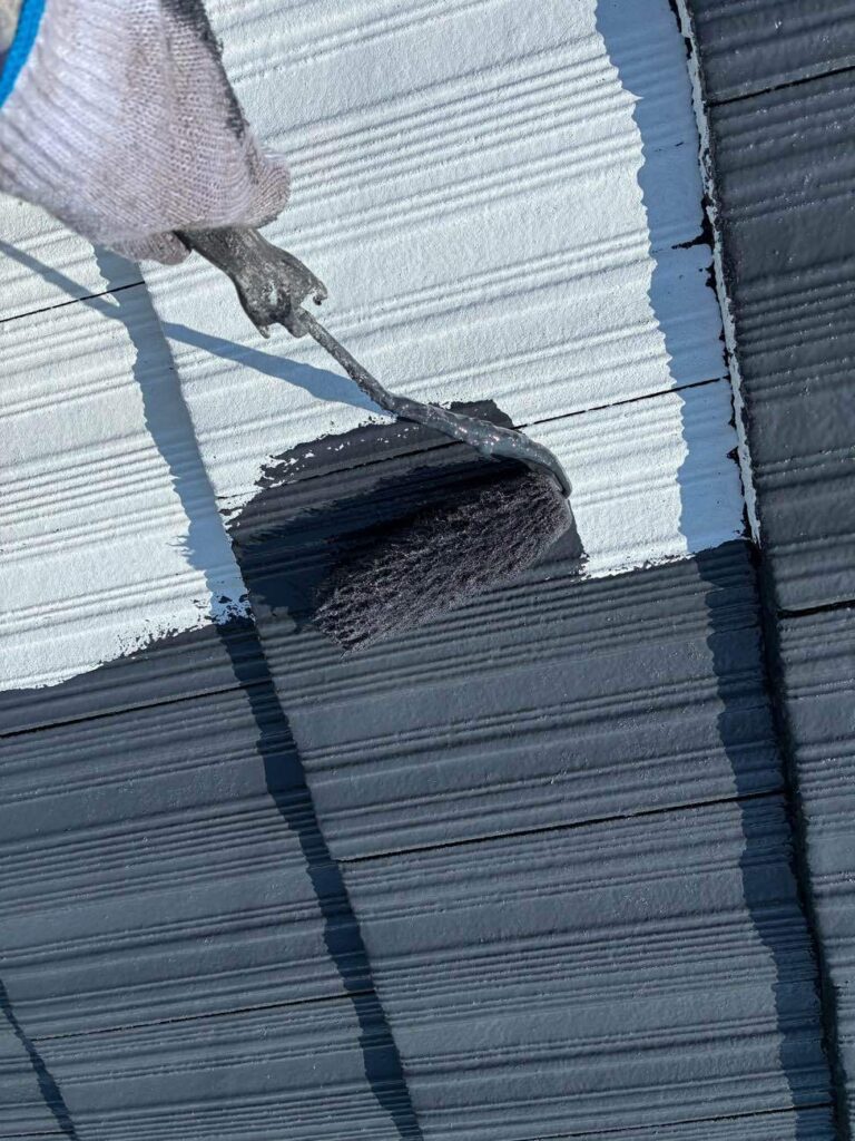 屋根の中塗りを行う様子です。屋根の中塗りには、主に塗膜の厚みを増す、上塗りとの密着性を高める、色ムラをなくす、美観と耐久性を向上させるという4つの役割があります。これらにより、下塗りだけでは不足している機能や美観を補い、屋根の保護性能を高めて、塗装の耐久年数を延ばします。