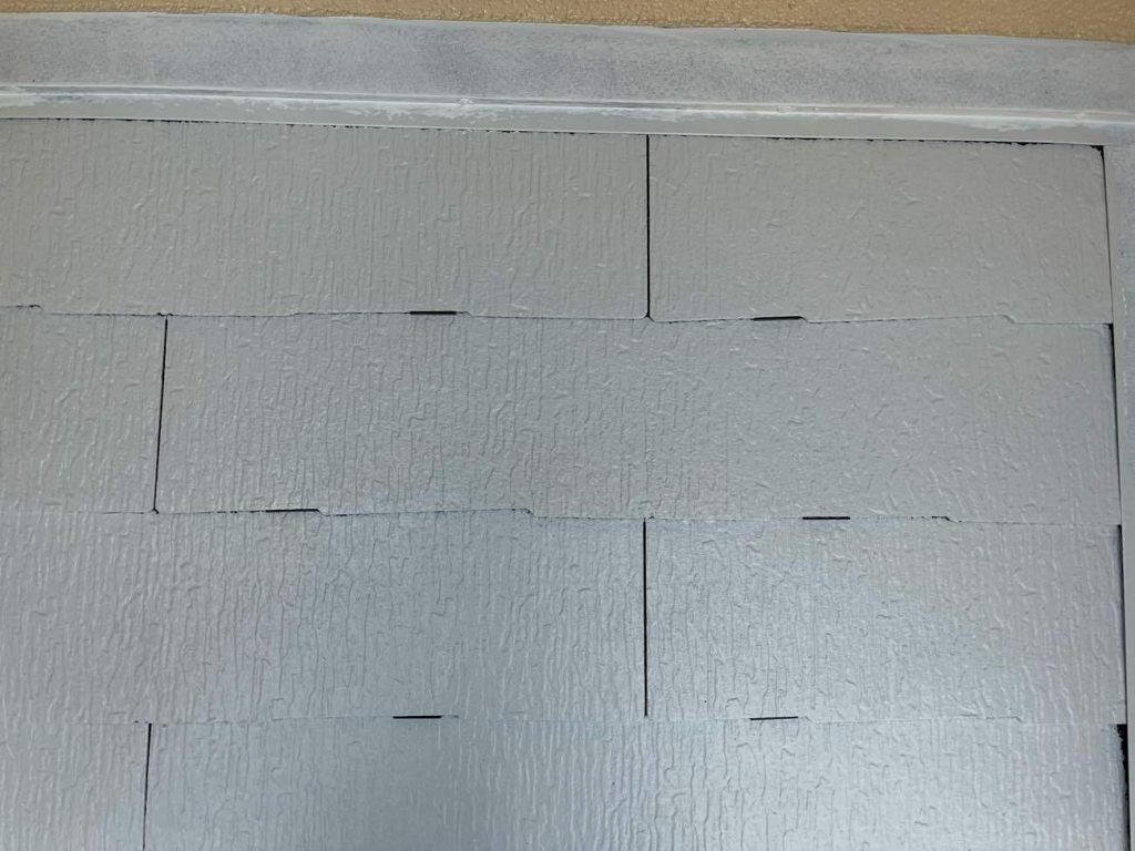 2回の下塗りが終わった後、タスペーサーを挿入します。タスペーサーにはシングル工法とダブル工法があり、ユウマペイントではダブル工法を採用しています。タスペーサーダブル工法とは、スレート屋根塗装で使われる「縁切り」という工程の一つで、1枚の約90cm幅のスレート屋根材に対して、両端から15cm内側にタスペーサーを2個（左右それぞれ1個ずつ）挿入する方法です。これはタスペーサーの開発元が推奨する工法で、下塗り乾燥後に差し込み、塗料でスレートの隙間が塞がってしまうのを防ぎ、雨漏りや瓦の割れを防ぐ目的があります。90cm幅の屋根材は、塗装で隙間が塞がりやすいため、より確実に縁切り（隙間を確保）するために2個挿入するダブル工法が推奨されています。