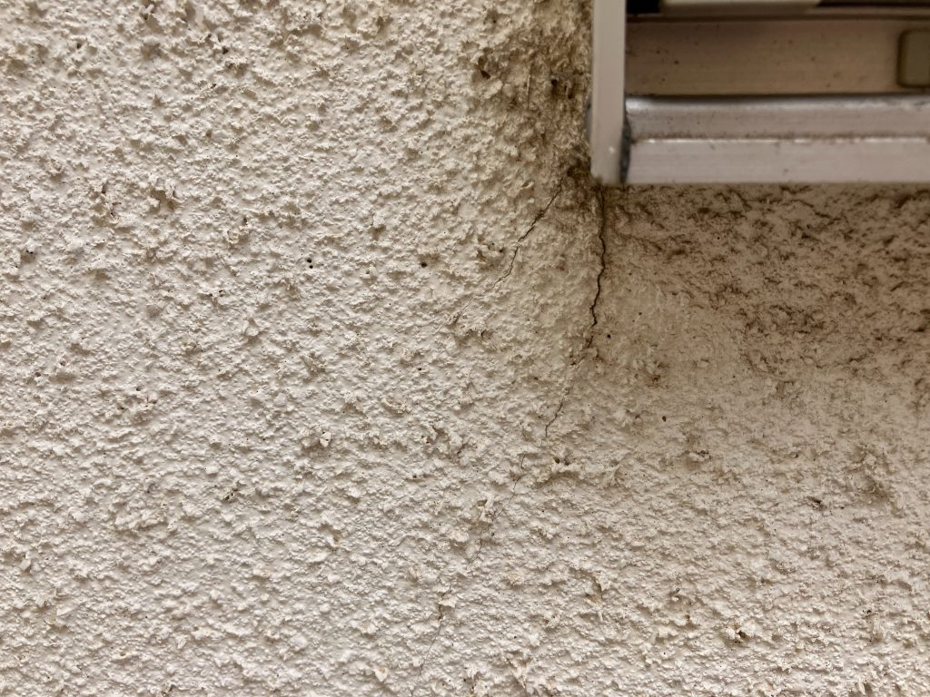 サッシまわりからひび割れが発生しています。モルタル外壁によく現れるひび割れ（クラック）。経年劣化はもちろんですが、地震や交通振動、地盤の弱さなどで建物がわずかに動くと、 壁の一部に力が集中してひび割れが発生します。