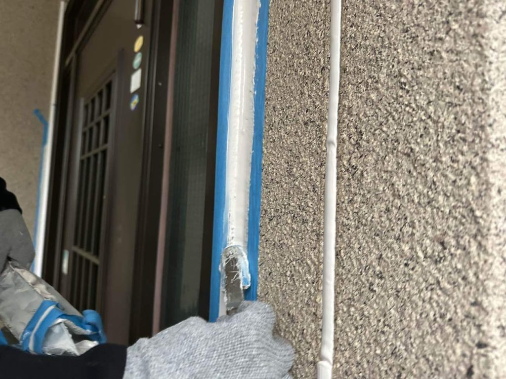 玄関まわりのシーリングを撤去し、新しいシーリング材を充填してならしている写真です。目地部分のシーリング材注入の写真です。シーリング材はサンライズ SRシールH100を使用します。紫外線耐侯が高く、シーリングに重要な柔軟性の高さが特徴です。