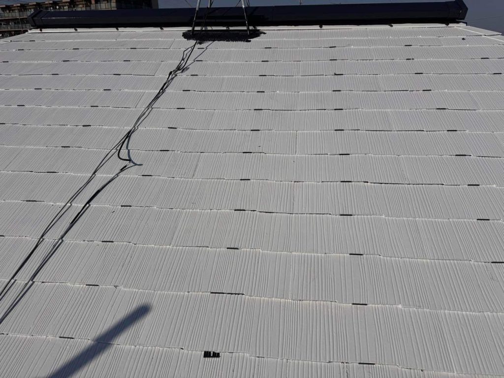 タスペーサーを挿入する様子です。タスペーサーにはシングル工法とダブル工法があり、ユウマペイントではダブル工法を採用しています。タスペーサーダブル工法とは、スレート屋根塗装で使われる「縁切り」という工程の一つで、1枚の約90cm幅のスレート屋根材に対して、両端から15cm内側にタスペーサーを2個（左右それぞれ1個ずつ）挿入する方法です。これはタスペーサーの開発元が推奨する工法で、下塗り乾燥後に差し込み、塗料でスレートの隙間が塞がってしまうのを防ぎ、雨漏りや瓦の割れを防ぐ目的があります。90cm幅の屋根材は、塗装で隙間が塞がりやすいため、より確実に縁切り（隙間を確保）するために2個挿入するダブル工法が推奨されています。