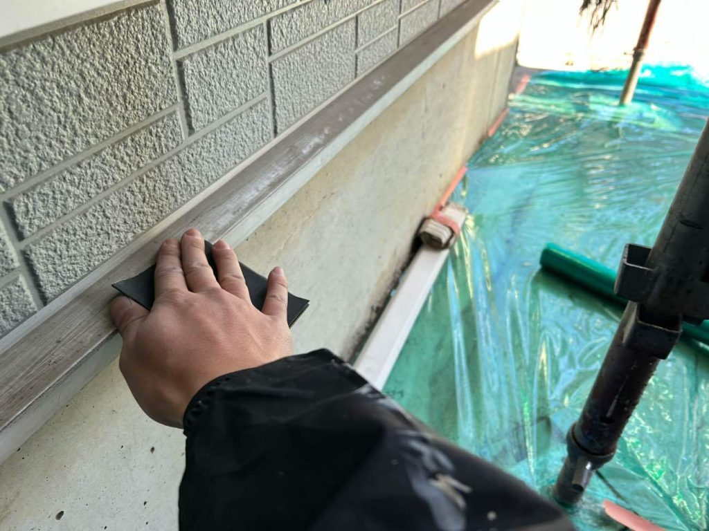 基礎とサイディング外壁の間にある水切り（鉄部）のケレン（研磨）作業をしている様子です。水切りも鉄部のためケレンを行い、塗料の密着をよくします。