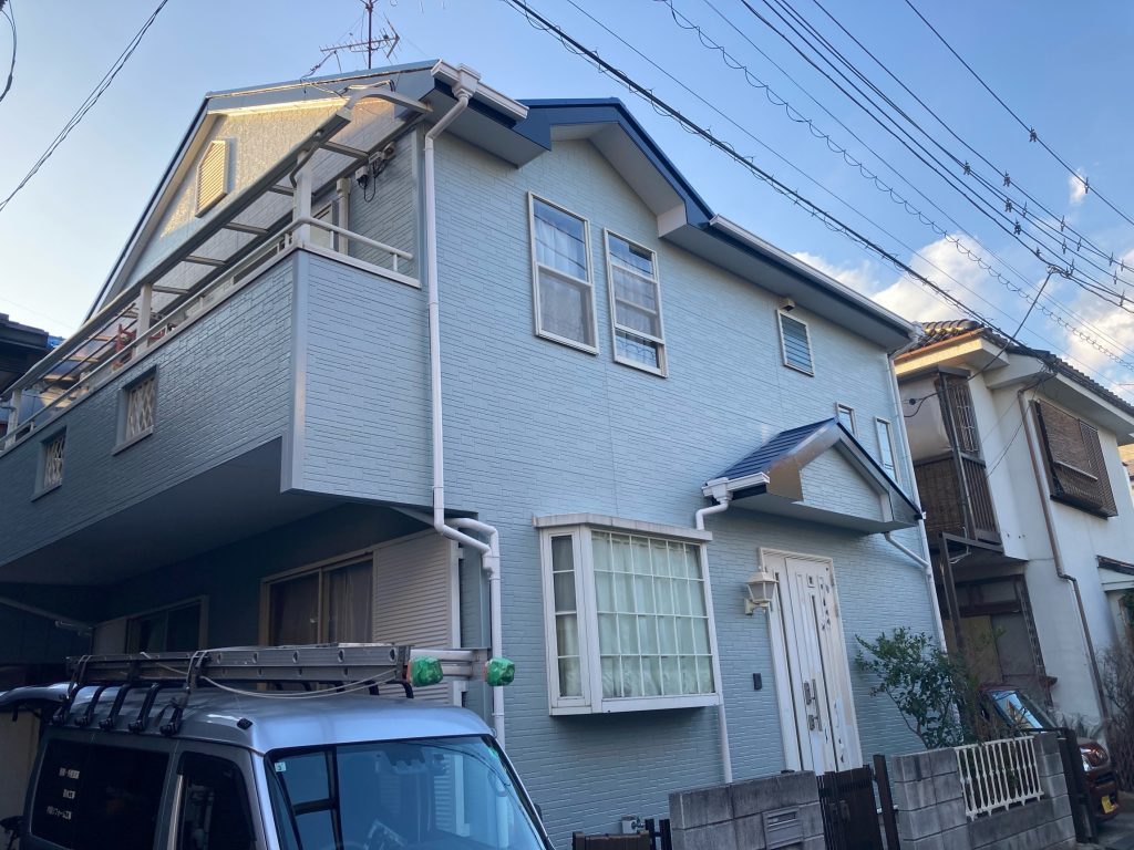 施工完了後の全景写真です。外壁は日本塗装名人社の「UVアクアコート（色番号SC-29）」で塗装しました。紫外線による劣化（チョーキング）を抑え込む先進的なフッ素塗料です。屋根の濃いブルーとのコントラストが美しいだけでなく、塗膜表面の「親水性（水になじみやすい性質）」によって雨水が汚れの下に入り込んで洗い流してくれるため、長期間にわたって綺麗なお住まいの外観を保ちます。