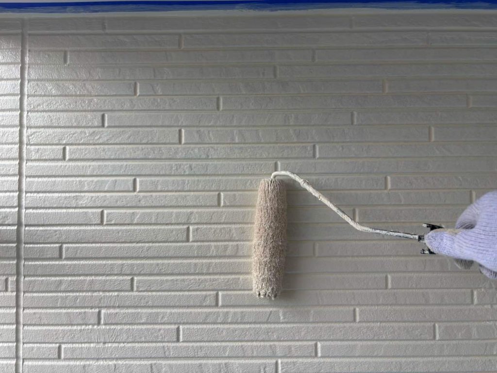 外壁の中塗りを行います。中塗りは、塗膜の厚みを増して耐久性や保護機能を高めるための重要な作業です。一般的に上塗りと同じ塗料を使用し、色ムラをなくし、上塗りの密着性を向上させ、均一で滑らかな下地を作ることを目的としています。どんなに高機能な塗料を選んでも、中塗りの施工が雑だったり適当な作業になってしまうと、本来の機能を果たせないまま早期剥離などにつながる可能性があります。今回使用した塗料はアステックペイント 超低汚染リファイン1000MF-IR（8091ブロークンホワイト）です。