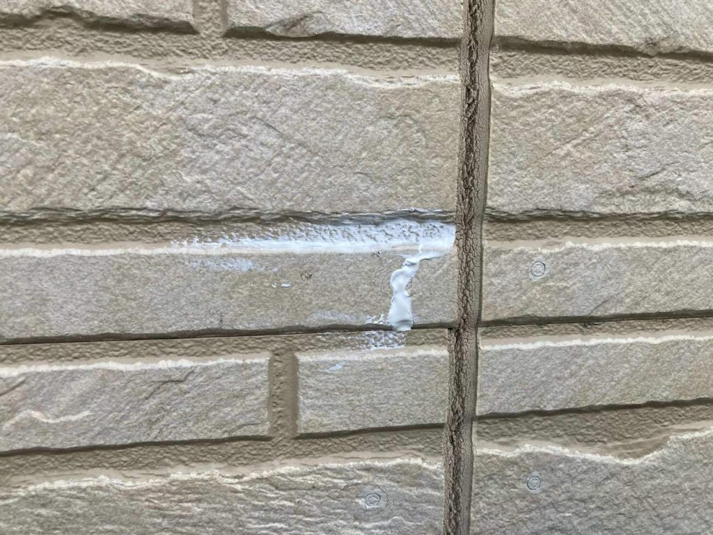 外壁塗装前の重要な工程である「下地処理」の様子です。サイディングのひび割れ部分にコーキングやパテを丁寧に充填し、補修しています。この丁寧な補修作業が、塗料の密着性を高め、お住まいを長持ちさせるための大切な土台となります。