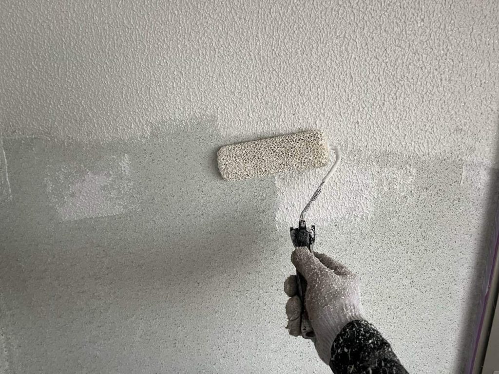 続いて、下塗り2回目の工程です。日本ペイントのアンダーフィラー弾性エクセルを使用し、専用の砂骨ローラーを用いてさざ波模様をつける「砂骨仕上げ」で塗布します。微弾性を持つ肉厚なフィラーを重ねることで、モルタル表面のひび割れを追従して埋め、外壁に立体感のある美しい質感を与える重要な工程です。