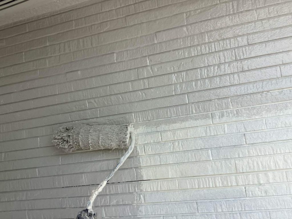 下塗りが乾燥した後、日本塗装名人社の日本塗装名人社無機UVコート水性で中塗りを行います。色は明るく温かみのあるライトクリーム（SC-32）です。メーカーの定める基準塗布量を厳守し、ローラーを用いて外壁全体に均一な厚みを持たせて塗り広げ、無機ハイブリッド塗料の超高耐候性を発揮させる強靭なベースを形成します。