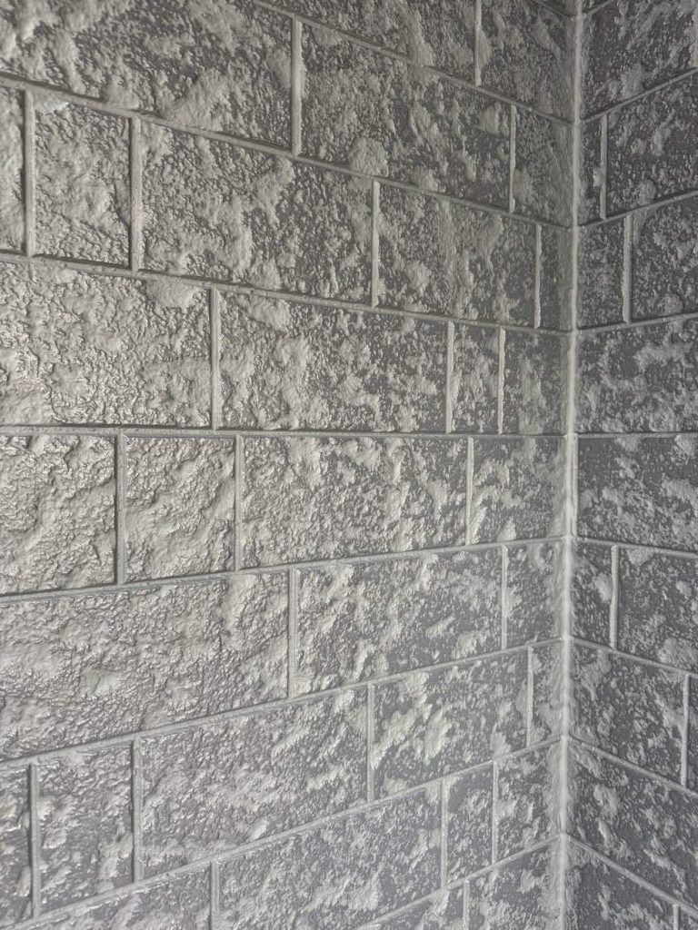 目地部分には明るめのグレー（SC-42 艶消し）を、表面の叩き部分には濃いグレー（SC-48 艶消し）を使用し、丁寧に塗り分けています 。高級感の演出： 単色（ベタ塗り）では失われてしまうサイディング本来の凹凸や石積みの風合いを活かし、アップの写真でもわかるように、立体的で非常に重厚感のある仕上がりを実現しました。