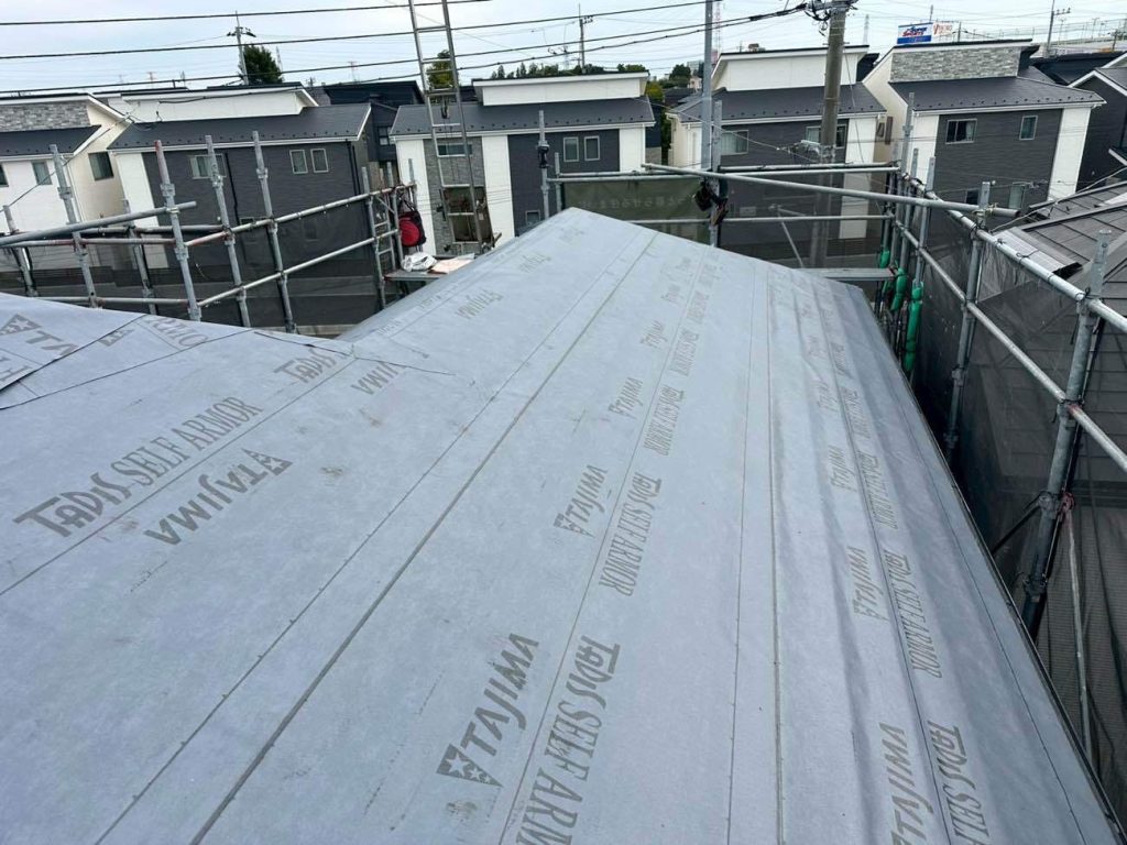 撤去後の屋根全面に、高機能防水シート「タディスセルフアーマー」を敷設します。このシートは遅延粘着型と呼ばれ、時間が経つほど下地に強力に密着し、釘穴からの雨水浸入を長期間防ぐ「自己修復性」を備えています。屋根カバー工法において、この防水シートは二次防水の要となる最も重要な部材です。軒先から棟に向かって隙間なく丁寧に貼り込むことで、既存の屋根材との間に強固な防水層を形成し、将来にわたる雨漏りのリスクを根本から防ぎます。