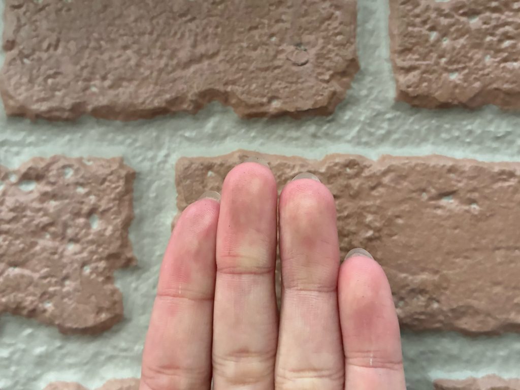 施工前の1階外壁（レンガ調サイディング）の様子です。<br /><br />外壁を手で触って劣化状態を確認する「触診」を行っているところです。指先に白い粉が付着する「チョーキング（白亜化）現象」は起きておらず、塗膜の防水機能はまだ完全に失われていないことが確認できました。また、建物の北側など日が当たりにくい面を中心に、日陰特有のコケやカビの発生がないかもしっかりと調査しましたが、幸いにも目立った発生は見られませんでした。しかし、外壁全体の色あせや、レンガ調の風合いが薄れてきていることから、今後チョーキングやコケの発生が始まる一歩手前の状態であると判断できます。このタイミングで、元の意匠性を活かす「グラデーション塗装」によるメンテナンスを行うことで、より良い状態を長く保つことができます。