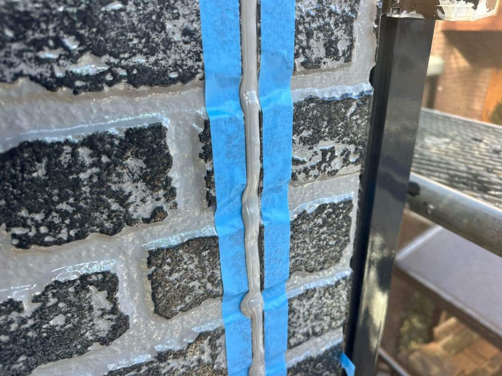 プライマー塗布後、新しいシーリング材を目地の奥まで隙間なく充填していく工程です。今回の施工では、紫外線に強く長期間にわたって高い柔軟性を維持できる高耐候仕様のシーリング材（サンライズ社 高耐候シールH100）を採用しています。専用のガンでたっぷりと注入した後、ヘラを使って表面を平滑に押し込みながら整えていきます。これにより、外壁材からの雨水の浸入を防ぎ、建物の揺れにもしっかりと追従する防水目地が完成します。