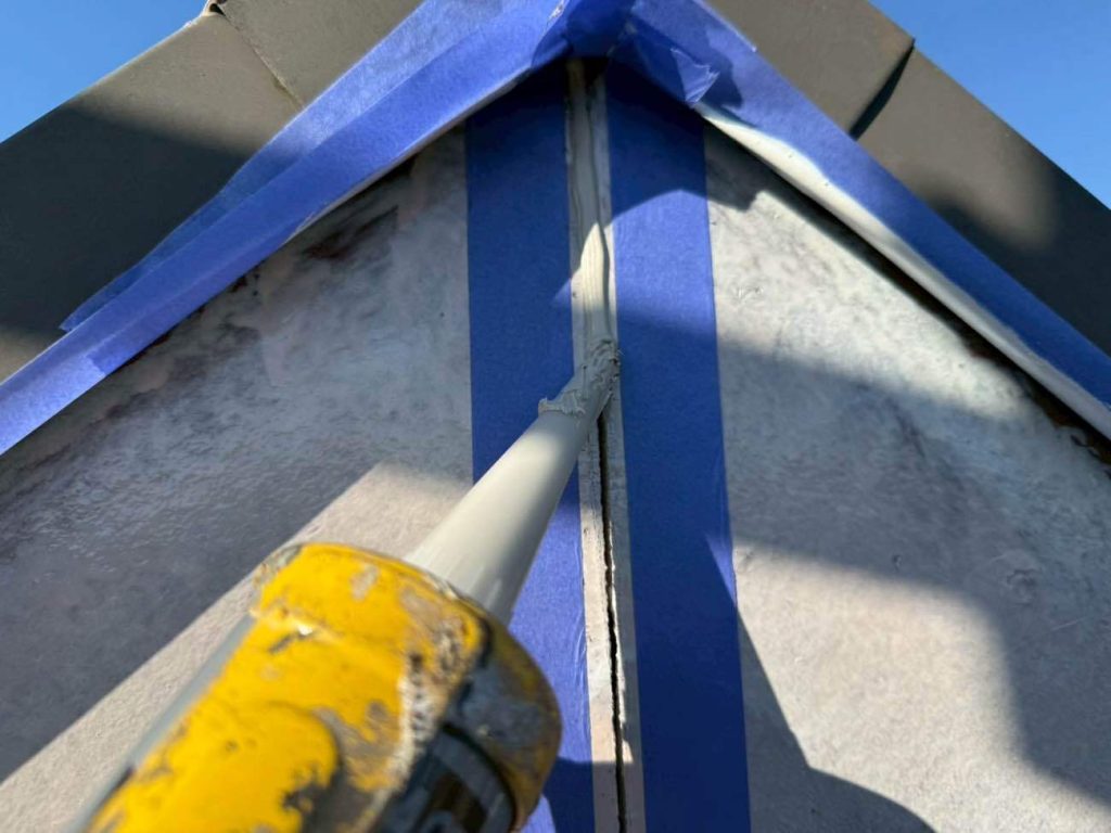 塗装の前に行う、破風板の板と板の継ぎ目のシーリング（コーキング）打ち替え工程です。屋根の側面にある破風板は、強風や紫外線を直接受ける過酷な環境にあり、建物の微細な揺れや寒暖差による素材の収縮といった負荷が継ぎ目に集中します。そのため、古いシーリング材が劣化してひび割れたり隙間ができたりすると、そこから雨水が内部へ浸入し、破風板自体の腐食や雨漏りに直結する危険性があります。今回の施工では、傷んで硬くなった既存のシーリング材をカッターで根元から綺麗に撤去し、専用のプライマー（接着剤）を塗布した上で、新しい高耐久なシーリング材を隙間なくたっぷりと充填しました。上から塗装を被せる前に、まずはこの「見えない防水の要」を徹底的にやり直すことが、お住まいの寿命を大きく延ばすことに繋がります。