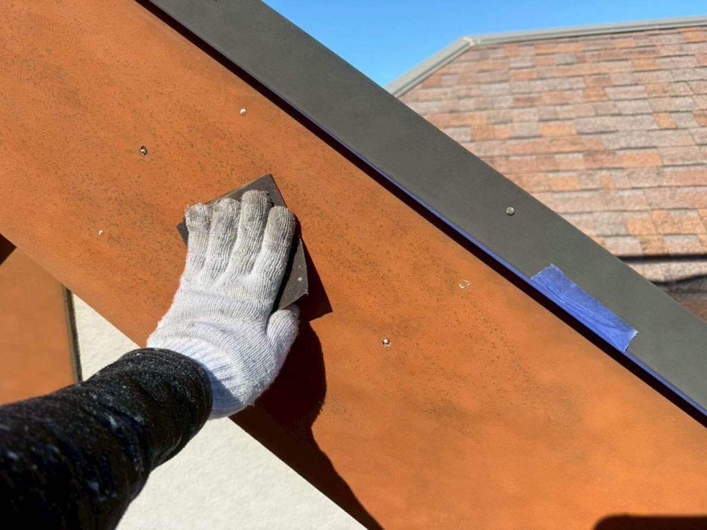 屋根の側面にある破風板（はふいた）の下地処理の様子です。ここは紫外線や風雨を直接受けるため、古い塗膜の劣化やひび割れが起きやすい過酷な部位です。まずはヤスリがけで傷んだ旧塗膜を徹底的に削り落とし、塗料を塗るための健康な下地を露出させます。削り終えた後は、木部やサイディング材の表面に残った細かな粉塵や見えない汚れをシンナーを含ませたウエス（布）で綺麗に拭き上げ、新しい塗膜が本来の耐久性を発揮できる環境を準備します。