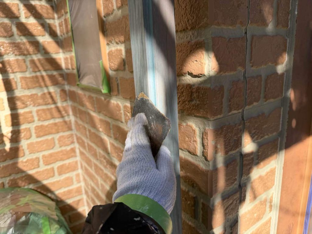 雨樋の塗装前に行う重要な下地準備です。雨樋は表面がツルツルとした素材（塩化ビニルなど）であるため、そのまま塗料を乗せてもすぐに剥がれてしまいます。そこで、専用の研磨材で表面にわざと細かな傷をつける「目粗し（ケレン）」を行い、塗料がしっかりと食いつくための足場を作ります。その後、静電気などで付着した頑固な排気ガス汚れや削りカスをシンナーで丁寧に拭き取り、塗料が完全に密着するクリーンな状態に整えます。