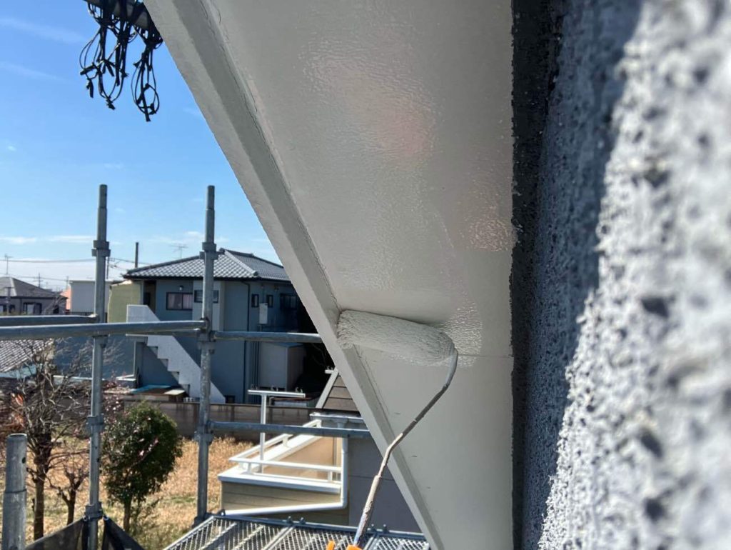 外壁からせり出した屋根の裏側にあたる、軒天井の下塗り工程です。軒天井は日陰になり湿気が溜まりやすいため、専用のシーラーを塗布して下地を整えます。この下塗り作業を行うことで、表面の劣化した素地を補強し、次に塗布する透湿性防カビ塗料の密着性を高めることができます。ローラーを用いて、端や隅に塗り残しがないよう均一に塗り広げていきます。