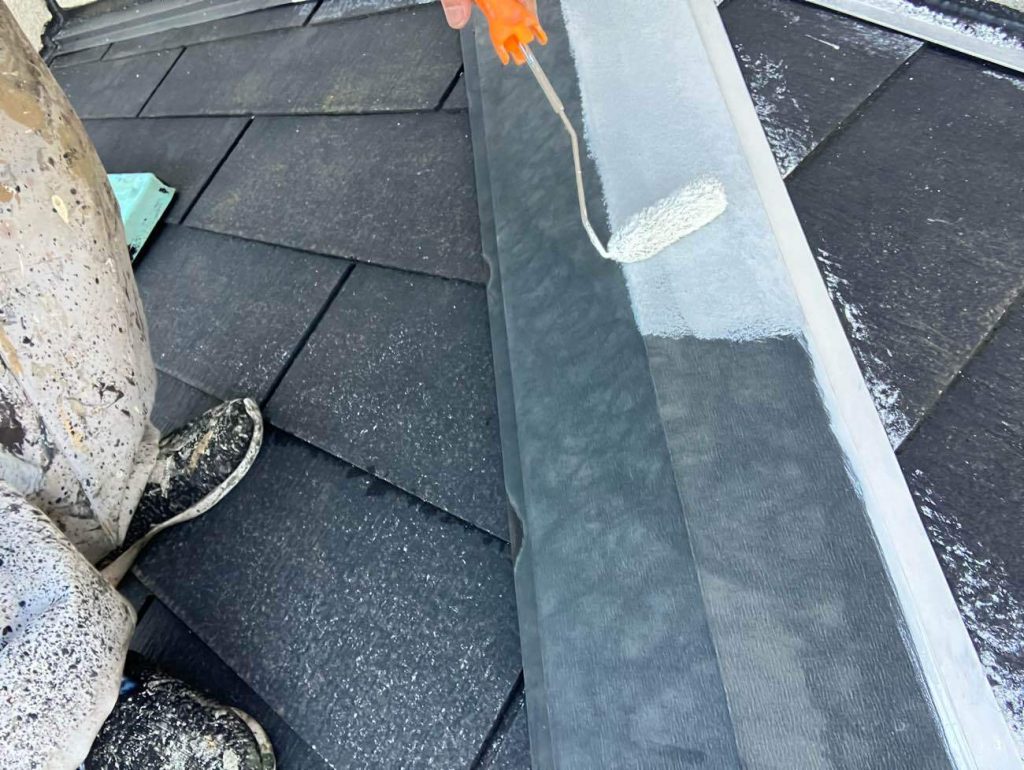 屋根の頂上部にある棟板金の下地処理および下塗り工程です。まずケレン作業により表面のサビや旧塗膜を研磨し、浮いている釘があれば打ち直して固定力を回復させます。素地を整えた後、金属専用の防錆効果のある錆止め塗料を塗布します。ローラーと刷毛を使い分け、板金の重なり部分や細部まで塗り残しがないよう丁寧に塗り込み、サビの腐食から長期間守るための強固な土台を構築します。下塗り後、日本塗装名人社 フッソUVコート溶剤を中・上塗りをします。