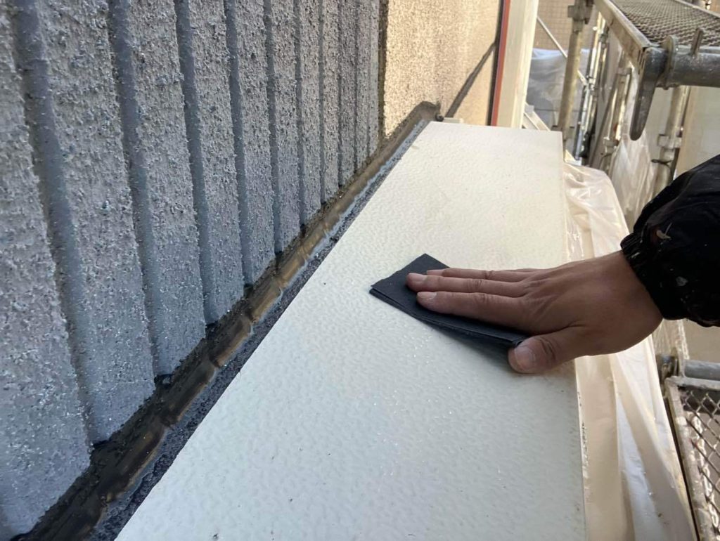 出窓上部に設置されている霧除け板金の下地処理です。太陽光や雨を直接受けるため劣化しやすく、旧塗膜の剥がれやサビが発生していました。サンドペーパーなどを使い、表面の旧塗膜やサビ、汚れを研磨して落とすケレン作業を行います。この作業には、表面を平滑に整えるとともに、微細な傷をつけて新しい塗料の密着を高める効果もあり、塗装の耐久性を左右する重要な工程となります。