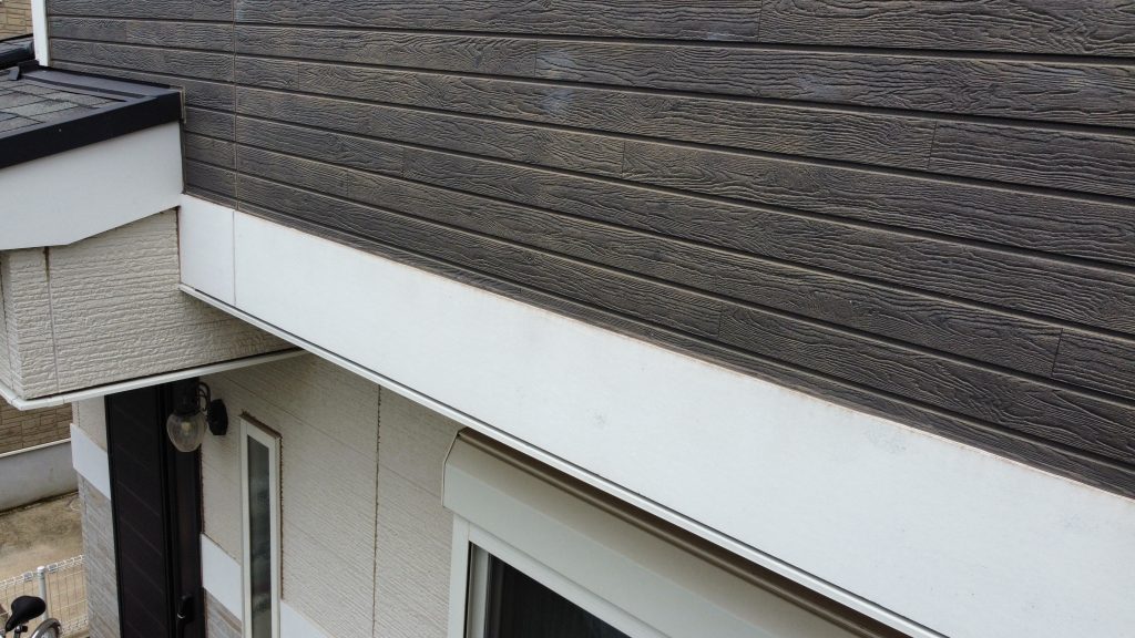 木目調やタイル調など、意匠性の高いサイディング外壁の施工前の様子です。塗膜の劣化により表面の防水性が低下し、雨水を弾きにくい状態でした。特にパネル同士を繋ぐ目地のシーリング部分はひび割れや肉痩せが発生しており、放置すると外壁材の反りや内部への雨水浸入に繋がるため、古いシーリングを撤去して新しく打ち替える防水の要となる下準備が必須です。