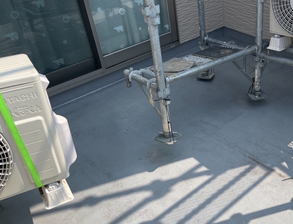 ベランダのFRP防水工事の最初の工程である下地処理です。床面に付着した砂埃や汚れを清掃した後、サンドペーパーなどを用いて既存の防水層の表面を研磨するケレン作業を行います。表面を平滑に整えると同時に、微細な傷をつけて次に塗る下塗り材の密着性を高める重要な工程です。下地をしっかりと整えることで、新しい防水層の膨れや剥がれを防ぎます。