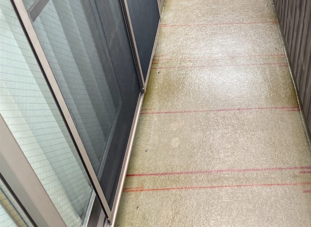 プライマー乾燥後、防水層を形成する工程です。今回は「1プライ仕様」での施工となります。補強材であるシート状のガラスマットを床面全体に敷き詰め、その上から防水用ポリエステル樹脂（中塗り）を塗布してマットに含浸させます。専用の脱泡ローラーを使って内部の気泡を丁寧に抜き取りながら下地と密着させることで、水を通さない強靭な防水層を形成します。