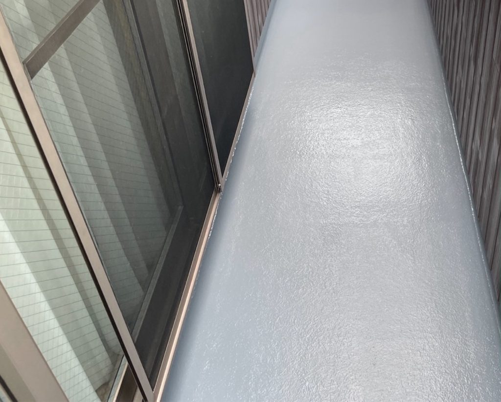 防水層が硬化した後、仕上げとなるトップコートを塗布する工程です。FRPの防水層そのものは紫外線に弱く、そのままでは太陽光で劣化が進行してしまいます。そのため、表面をコーティングするグレー色のトップコート（保護塗料）を全体にムラなく塗布します。美観を美しく整えるとともに、紫外線や歩行時の摩擦から防水層を長期間保護し、雨漏りを未然に防ぎます。