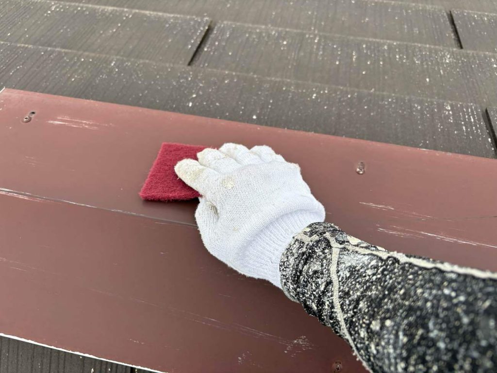 屋根の棟板金の下地処理の様子です。サンドペーパー等を用いて、板金をケレン（目粗し）を行います。ケレン後はシンナー拭きを行い細かい汚れなどを落とします。塗料の密着を良くするために必要な工程の一つです。
