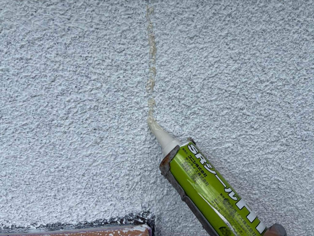 モルタル外壁のひび割れをコーキングやパテで丁寧に補修し、幕板上部の劣化したシーリングを高耐候な「サンライズH100」で打ち替えます。
