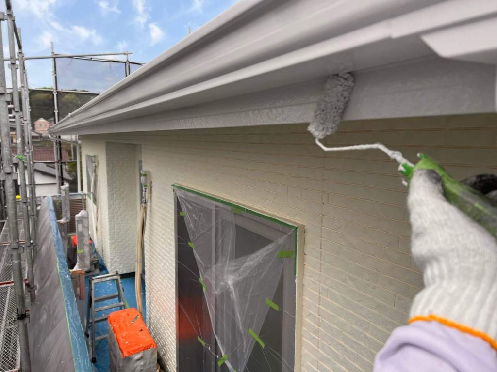 屋根の側面を保護する破風板の塗装工程です。紫外線や雨風のダメージを直接受ける過酷な部位であるため、まずは下塗り材の「シーラー」をたっぷりと吸い込ませて下地を強固に補強します。続いて、外壁用と同等の耐久性を持つ最高ランクの塗料「日本塗装名人社 無機UVコート溶剤」で中塗り・上塗りを施し、強靭な塗膜を形成します。外壁だけが長持ちしても、後から破風板の劣化で足場を組むことになっては意味がありません。部位ごとの耐用年数を外壁としっかり同調させることで、将来のメンテナンスコストを抑えます。