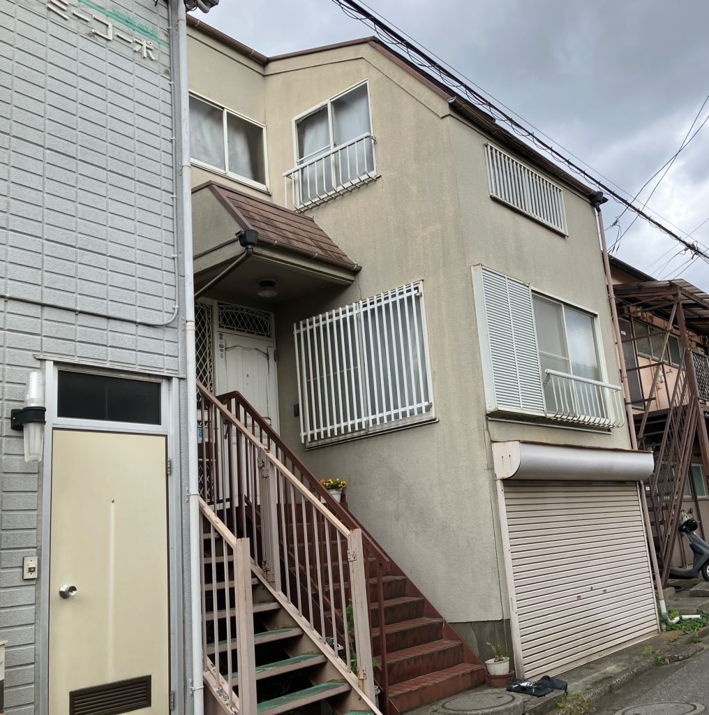 施工前の全景写真です。外壁全体にコケの発生や汚れの付着が広がっているほか、各所に大小のひび割れ（クラック）が見受けられる状態でした。